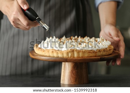 Woman toasting meringue on lemon pie with kitchen torch at table, closeup