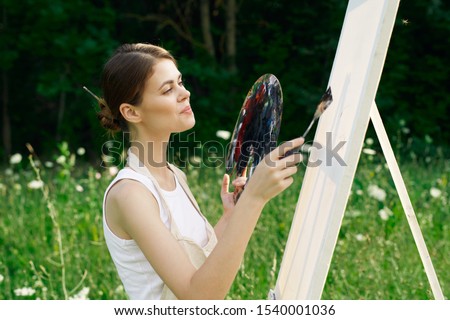 woman young beautiful model draws on nature on canvas
