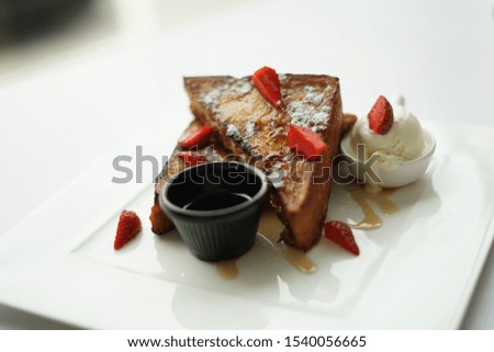Modern french toasts with  brown crust  with strawberries, honey drizzled and ice cream vanilla with a cup of tea on the side.