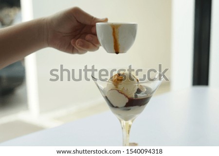 Female hand pouring coffee in the glass of affogato coffee: espresso shot with vanilla ice cream on white table, side view.