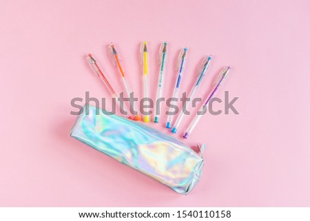 Gel pens of rainbow colors and a pearl pencil case on a pink background. Place for text, minimalism. The concept of school stationery, sketches, ideas.