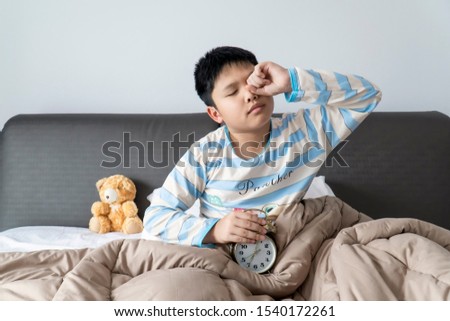 Asian boy reaching out for alarm clock on morning.