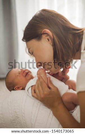 Close-up. Beautiful young mother kisses the baby. Beautiful young mother plays with the baby in bed.