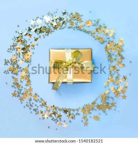 Luxury golden gift box around stars confetti as wreath on blue background. Christmas party. Flat lay. View from above. Xmas pattern.