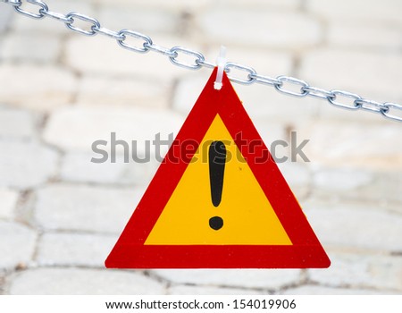 Bright red and yellow triangle exclamation mark hanging on metal chain