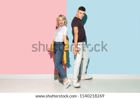Young emotional man and woman in bright casual clothes posing on pink and blue background. Concept of human emotions, facial expession, relations, ad. Beautiful caucasian couple dancing together.