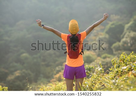 Woman ultramarathon runner outstretched arms to sunrise at tropical forest trail Royalty-Free Stock Photo #1540255832