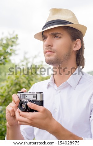Man with camera. Thoughtful young man holding camera in his hands and looking away