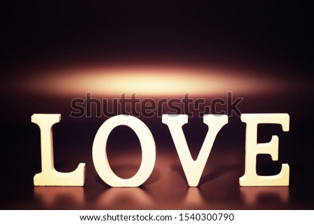 Wooden and metal letters forming word LOVE written on dark black background and lights.