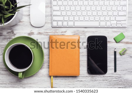 Top view designer table with office accessories. Morning coffee time and planning new day. Flat lay wooden desk with computer keyboard and mouse, smartphone, ruler, diary and green plant in pot.