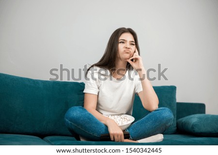 beautiful young woman cheers on her favorite team looking upset while watching football game eating popcorn on the sofa at home