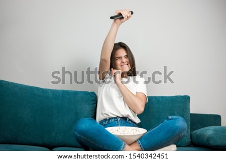 beautiful young woman with remote control in her hand cheers on her favorite team while watching football game eating popcorn on the sofa at home