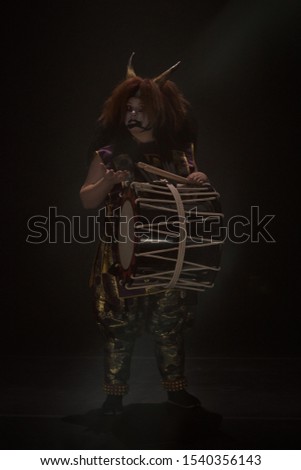 Taiko drummer in a wig and a demon mask on stage with drum on a black background. Surprised and indecisive question on the face. Demon from Japanese mythology.