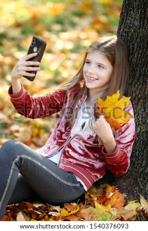 Beautiful girl taking selfie by smartphone in autumn city park