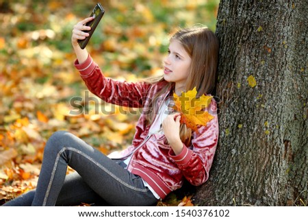beautiful girl taking selfie by smartphone at autumn park
