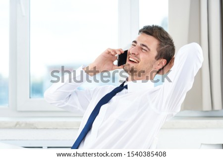 Happy man talking on a cell phone in his office and the window in the background