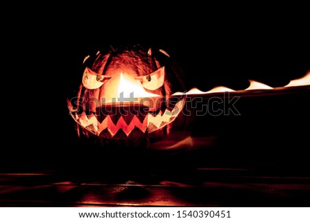 Carved spooky halloween pumpkin with glowing hot fire flame face. Big helloween autumn symbol with mad face, glowing eyes, mouth and teeth. Scary hot nightmare horror with evil smile at october 31st
