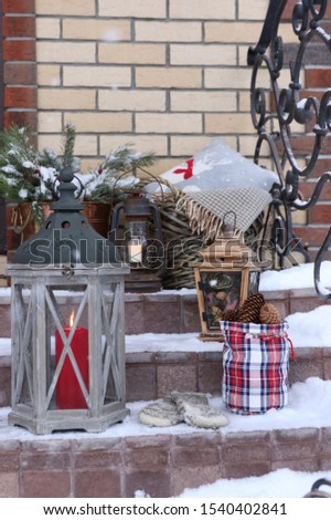 Winter scene with wooden candlestick, lantern, cones, wicker basket, wool plaid, knitted mittens, vintage cooper pot with branches of pine, old rusty oil lamp on stone steps, outdoor and space