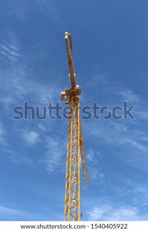 Construction high rise tower crane yellow stands alone against the bright blue sky
