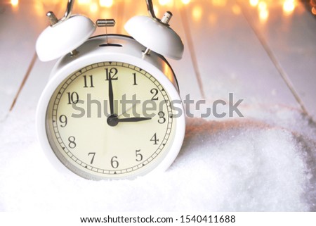 Time change in autumn. Alarm clock in the snow with fairy lights in the background