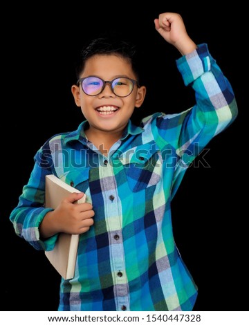 Asian handsome boy model wearing blue shirt, standing and holding a book, feeling happy smiling on black background. Photo shooting for education concept, happy learning school. Look clever and smart.