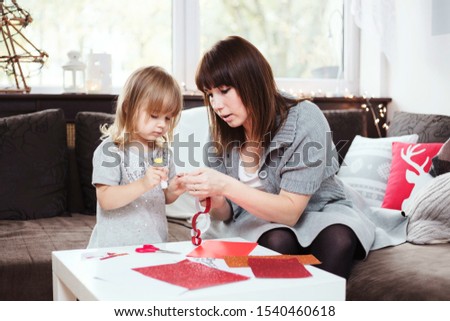 Mother and daughter making a Christmas paper chain with red and gold glitter paper. Lifestyle image, shallow depth of field.	