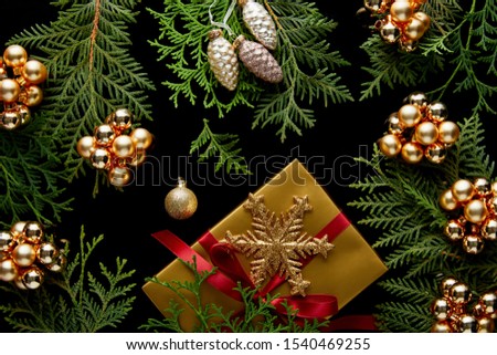 top view of shiny golden Christmas decoration, green thuja branches and gift box isolated on black