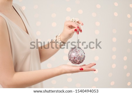Christmas decoration, ball in female hands close-up. White background with blurry lights of a garland.