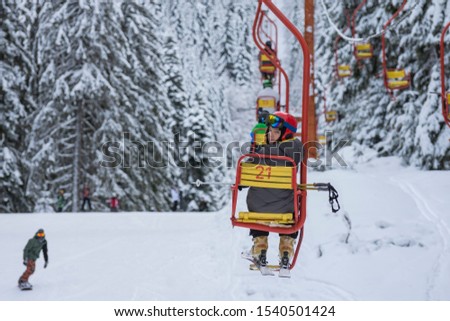 Skier, who sitting at old fashioned one chair ski lift, looks back.Chair ski lift next to slope for skis and snowboards. Ski area in snowy high mountain. Sports and recreation concept. Selective focus