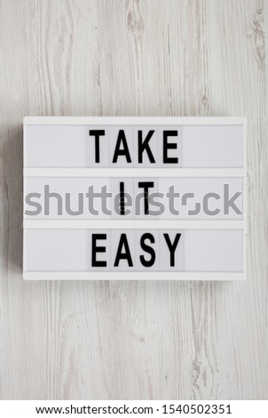 'Take it easy' words on a lightbox on a white wooden background, top view. Overhead, from above, flat lay. Close-up.