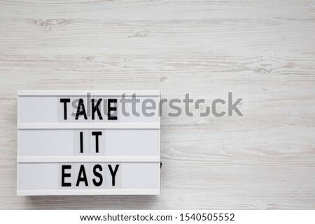 'Take it easy' words on a lightbox on a white wooden surface, top view. Overhead, from above, flat lay. Space for text.