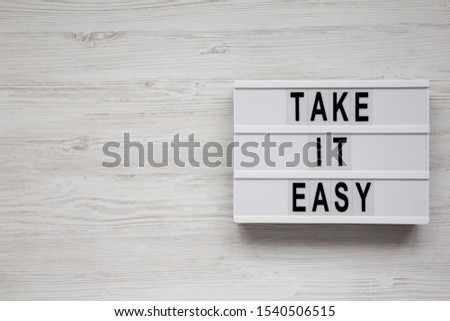 'Take it easy' words on a modern board on a white wooden surface, top view. Overhead, from above, flat lay. Copy space.