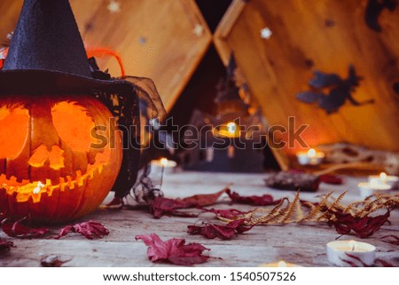 Close up carved pumpkin in witch hat with paper silhouettes of bats, castle, ghosts on wooden background. Head jack lantern with scary evil faces. Spooky holiday symbol, concept. Copy space