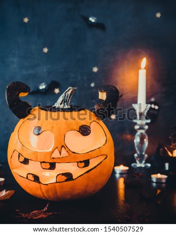 Carved luminous pumpkin with scary evil face, burning candles and paper silhouettes of bats, castle, ghosts on black stone background. Spooky holiday symbols and celebration concept. Vertical card