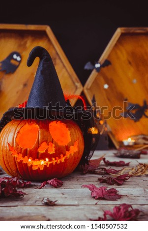 Close up carved pumpkin in witch hat with paper silhouettes of bats, castle, ghosts on wooden background. Head jack lantern with scary evil faces. Spooky holiday symbol, concept. Vertical. Copy space