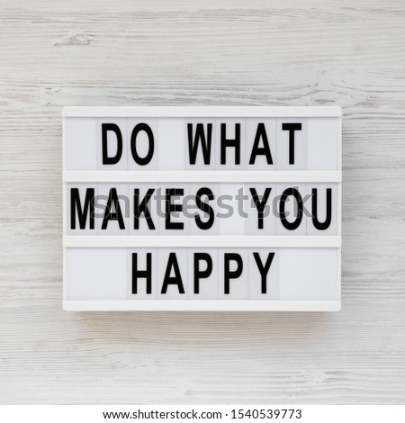 'Do what makes you happy' words on a lightbox on a white wooden surface, top view. Overhead, from above, flat lay. 