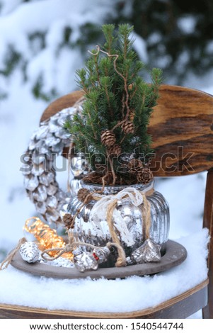 Winter composition with Christmas wreath, glass decoration, garland, fir tree, wooden star on vintage wooden child chair on snow, natural background, outdoor and space, scene in snow garden