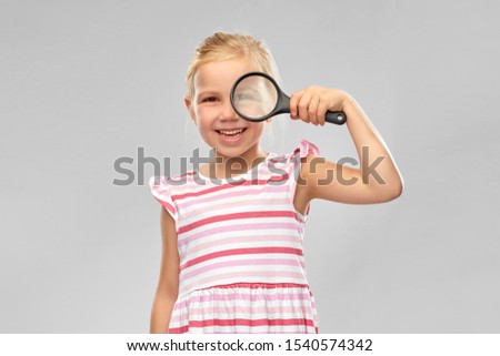investigation, discovery and vision concept - happy girl looking through magnifying glass over grey background