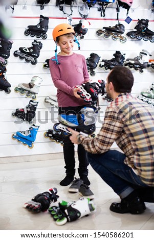 Smiling european male seller putting roller-skates on boy customer in sports store