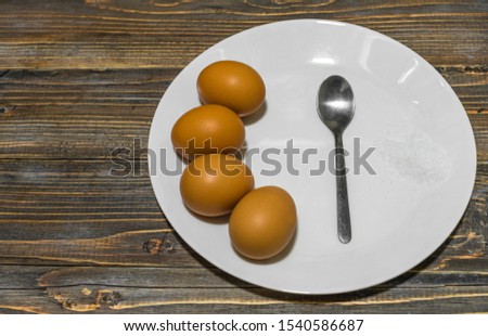 Boiled eggs, sea salt and a spoon on a plate standing on a wooden table. Close up. Copy space.