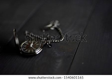 A closeup shot of an old black pocket watch on a black wooden surface with a blurred background
