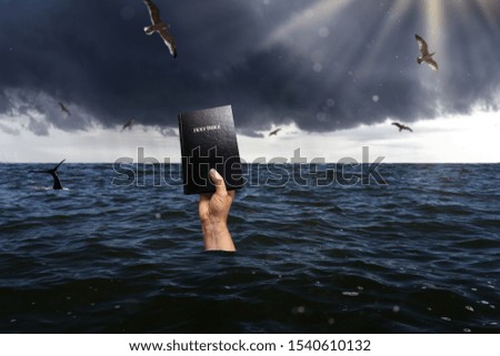 drowning person holding bible into the sky