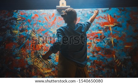 Talented Female Artist Works on Abstract Oil Painting, Using Paint Brush She Creates Modern Masterpiece. Dark and Messy Creative Studio where Large Canvas Stands on Easel Illuminated. Royalty-Free Stock Photo #1540650080