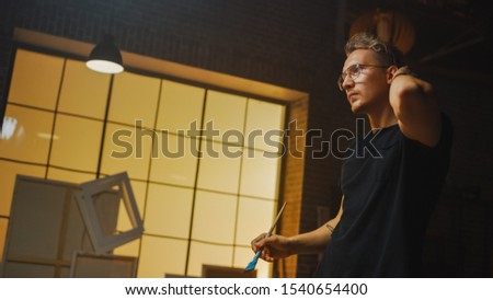 Portrait of Artist Working on Abstract Painting, Uses Paint Brush To Create Daringly Emotional Modern Picture. Dark Creative Studio Large Canvas Stands on Easel Illuminated. Side View Close-up Shot 
