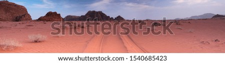 Panorama of Wadi Rum desert in early morning. Red sand and car tire tracks and mountains background