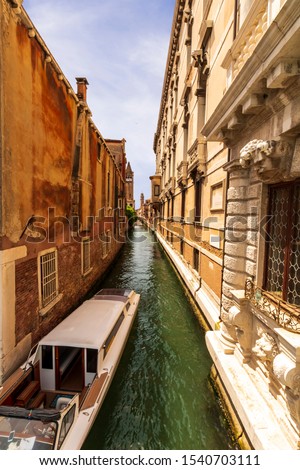 picturesque view at a narrow Venice chanel with boat, nice old builginds behind , church and beautiful sky on the background of the landscape