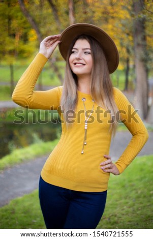 beautiful woman wearing fashion yellow sweater and brown hat walking in park and smiles. autumn season 