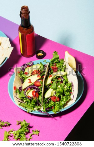 Healthy mixed salad on unwrapped tortilla, pink tabletop and blue background. Abstract healthcare conception.