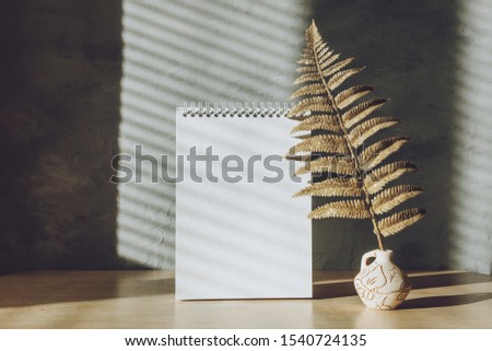 Modern trend home decor mockup with shadows and golden leaves. Fall autumn minimal mock up with open empty note pad, golden fern leaves and candle on grey concrete wall background