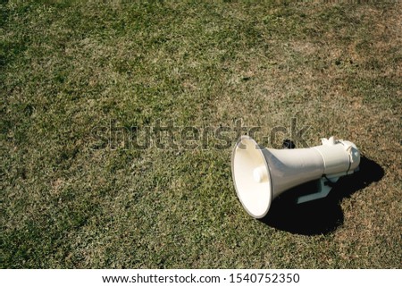 Overhead view of green digital megaphone left on the green vivid grass during social protest